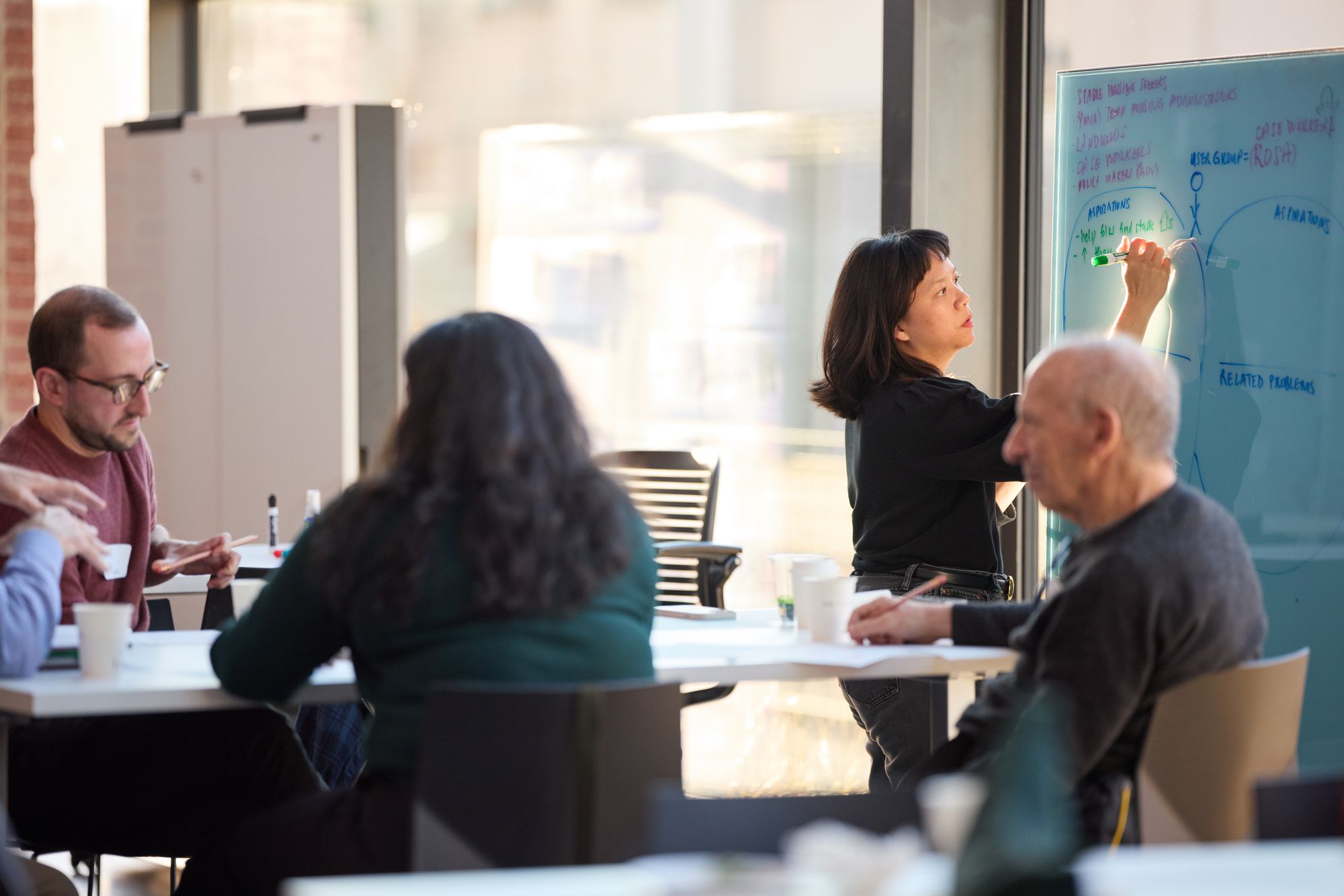 A group at work, one person writing on the whiteboard, others examining their notes.